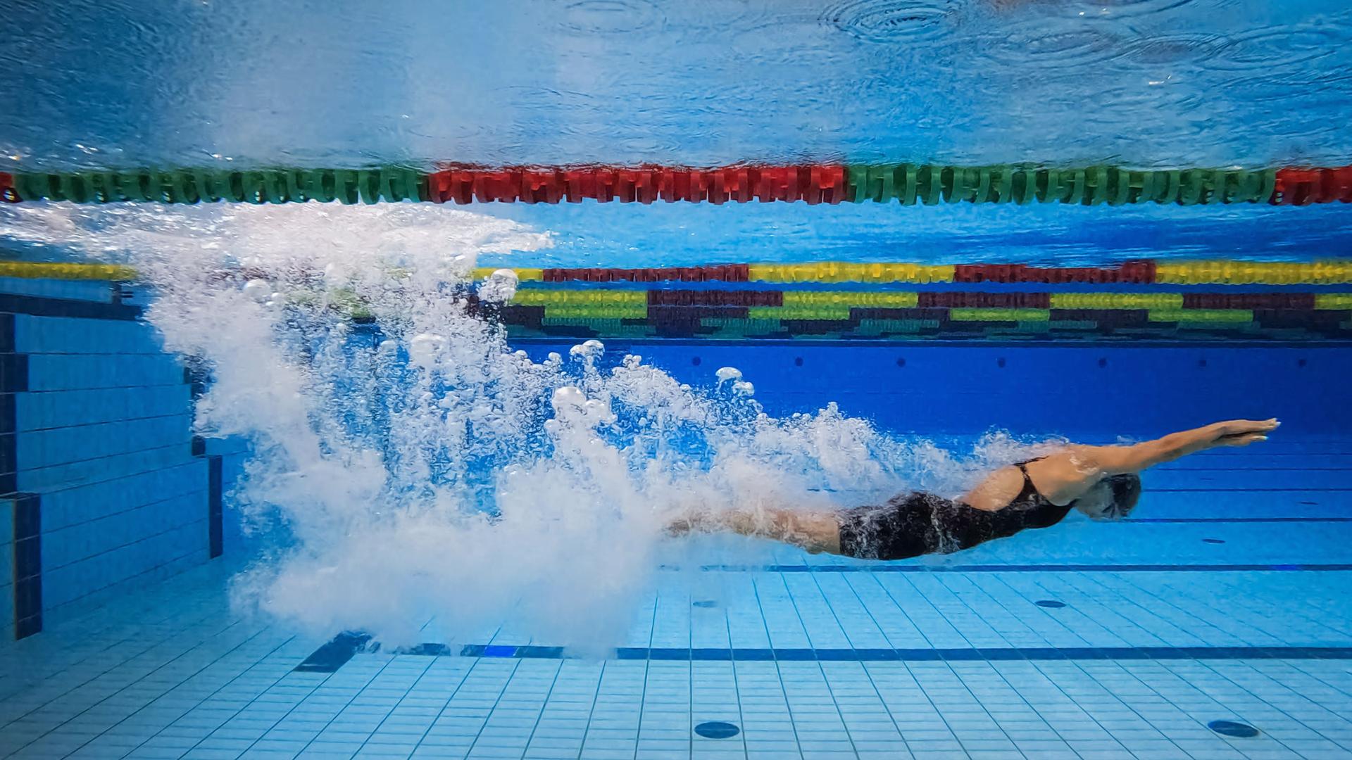 Female swimmer immersing and sliding below the water, underwater
