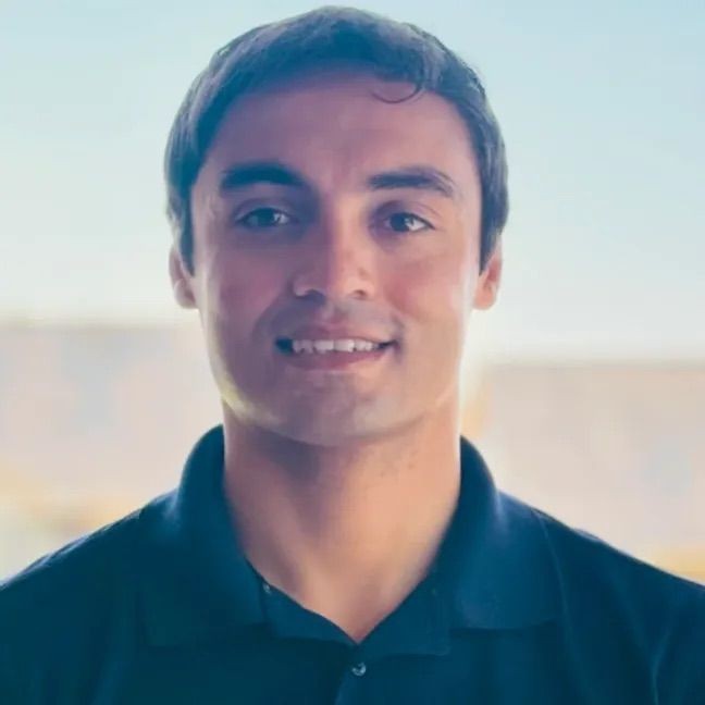 Smiling man in a dark polo shirt against a blurred background.