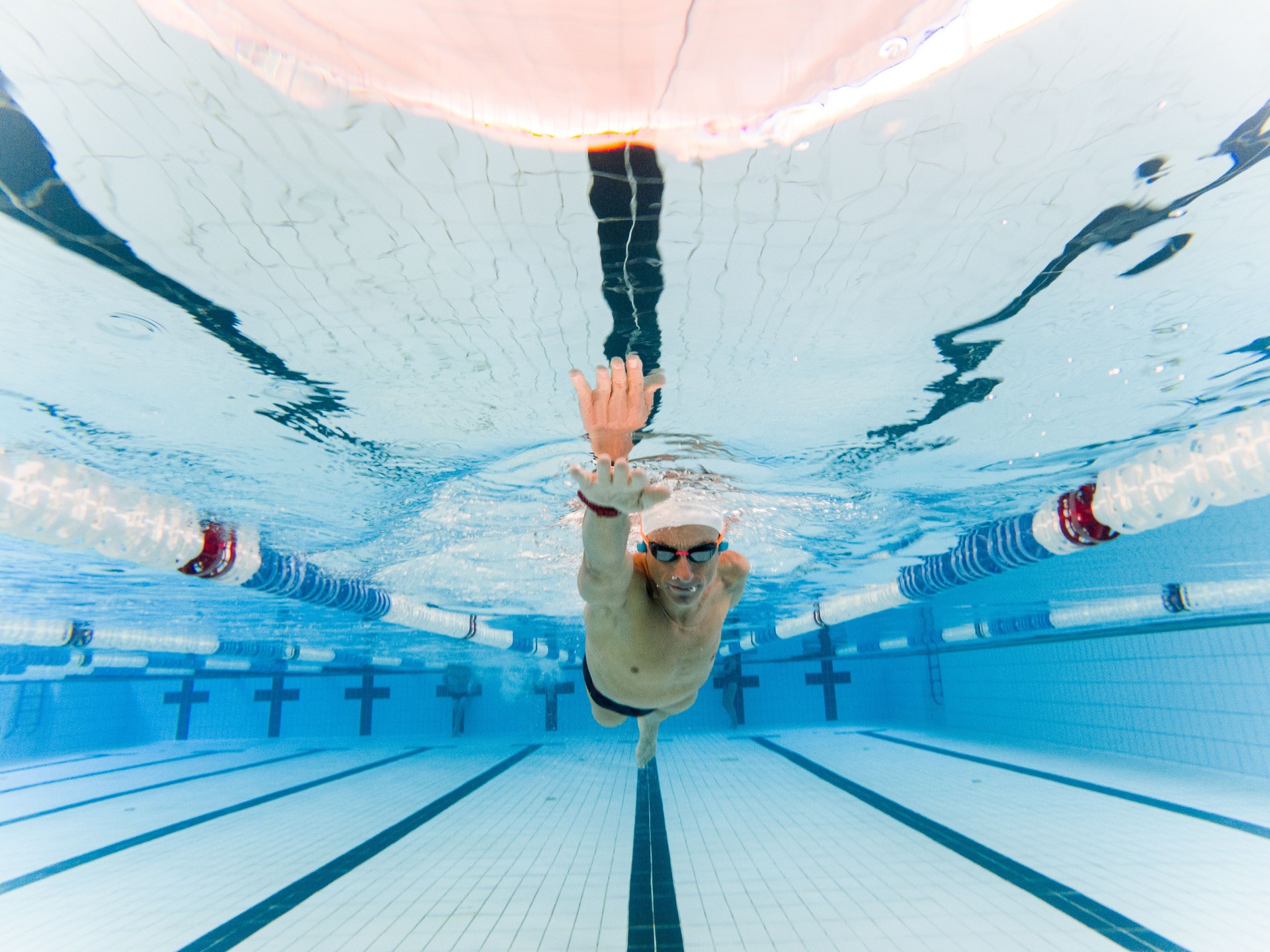 Underwater frontal photo of an adult male with an amputated arm swimming in an indoor pool. Disabled swimmers, athletes with an amputated arm. Motivation and determination.