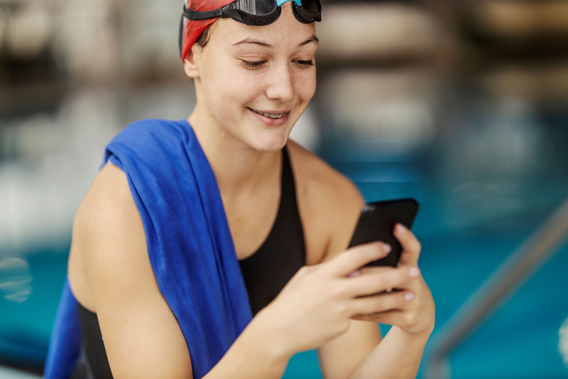 Portrait of a professional swimmer girl using a cellphone near pool.